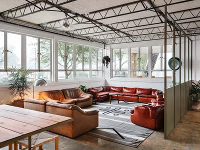 A spacious industrial living room with large leather sofas, concrete flooring, and exposed steel beams on the ceiling.