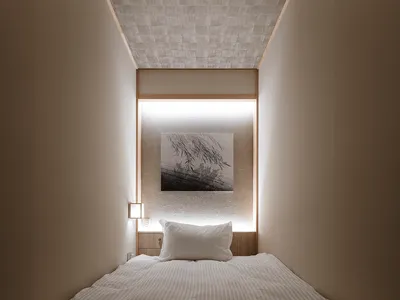 A minimalist bedroom with neutral-toned tiles, a single bed, and a framed artwork on the wall.