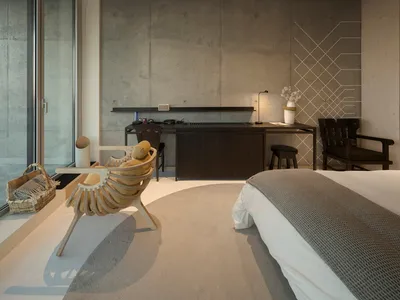 Modern minimalist bedroom with concrete walls, a large bed, and a sleek desk.