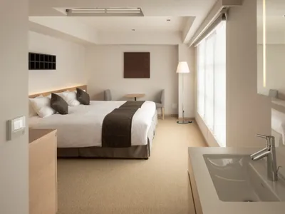 Modern, minimalist hotel room with a bed, nightstand, floor lamp, and sink with a silver faucet.