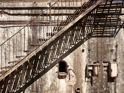 Rusted metal staircase on an abandoned industrial exterior with concrete walls.