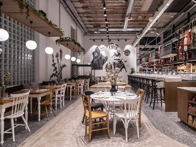 A modern cafe dining room with wooden tables, concrete flooring, and glass walls and shelves.