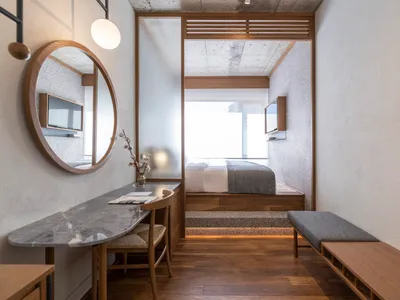 A minimalist bedroom featuring a concrete floor, wooden furniture, and a marble table with a vase of flowers.