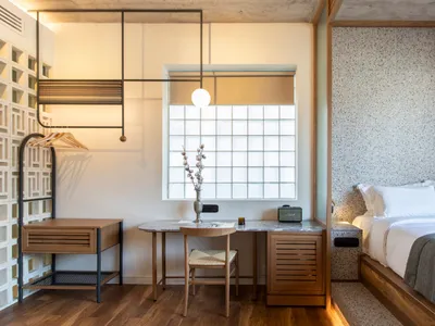 A minimalist bedroom features a horizontal window, wooden desk, and speckled terrazzo wall.