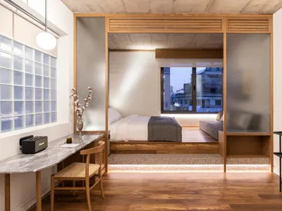 An elegant, minimalist bedroom featuring wood and glass materials, with a bed, desk, and a view of the city through frosted g