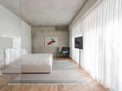 A modern minimalist bedroom with a concrete wall, white bed, and white curtains.