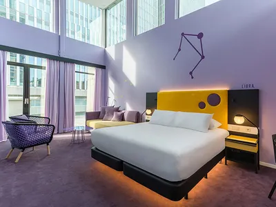 A modern bedroom featuring a purple bed with a yellow headboard, white duvet, and black nightstands.