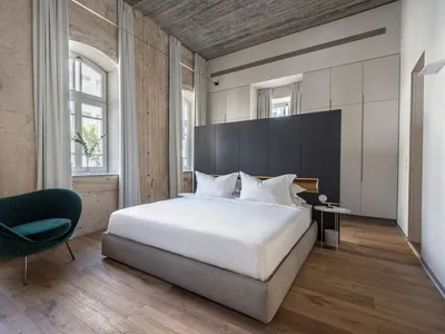 Modern minimalist bedroom with concrete walls, wood flooring, and a large window.