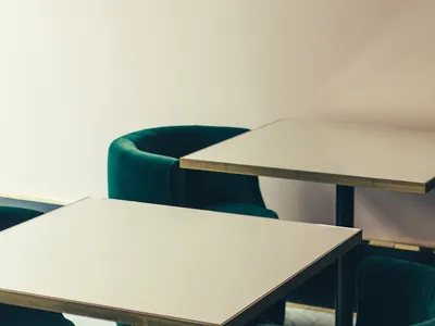 Minimalist restaurant interior with metallic accent lighting, green velvet upholstery, white walls and ceiling, and vinyl tab