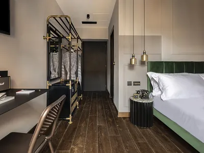 A modern bedroom featuring a green upholstered bed, wooden flooring, and brass accents.