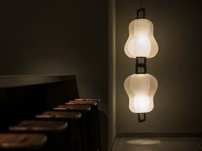 A row of stools in a dimly lit restaurant bar with a minimalist design, featuring a decorative paper lamp hanging from the ce