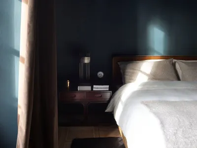 A minimalist bedroom with a white bed, wooden floor, and dark blue walls.