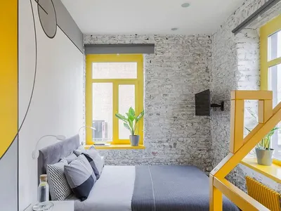 A modern bedroom featuring a concrete wall and wooden floor with a yellow window frame and a gray bed.