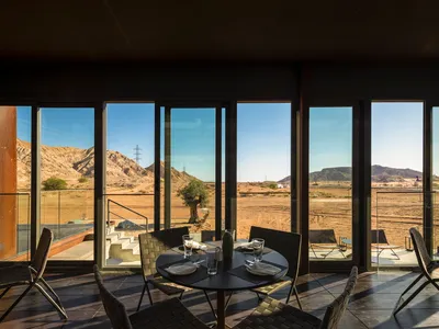 Modern restaurant interior with glass windows, metal dining furniture, and a view of the desert.
