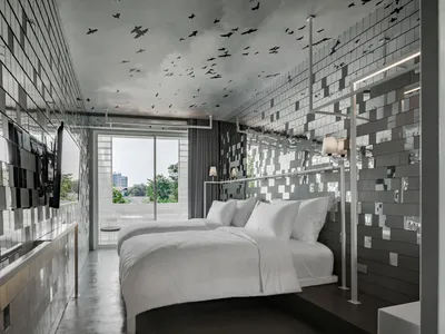 Modern minimalist hotel room with metallic mosaic tiles, bed with white bedding, and floor-to-ceiling windows.