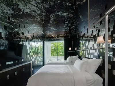 一間現代臥室，鋪設黑色鏡面瓷磚，窗外可見樹木景觀，雙人床鋪有白色床具，以及平整的