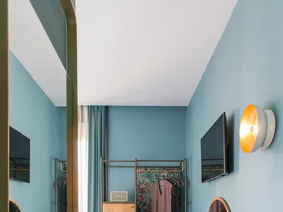 A minimalist bedroom with blue walls, wooden furniture, and a hanging wardrobe.