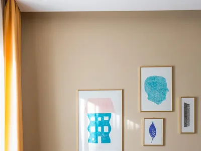A purple upholstered wingback chair in a well-lit bedroom with a yellow curtain, abstract art wall hanging, and a bed with a