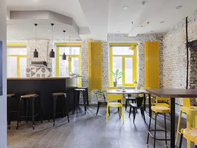A cozy cafe interior with yellow accents, featuring wooden floors, brick walls, and bright yellow decor.