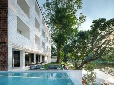 Modern hotel resort building with concrete exterior and outdoor seating area by a tranquil river.
