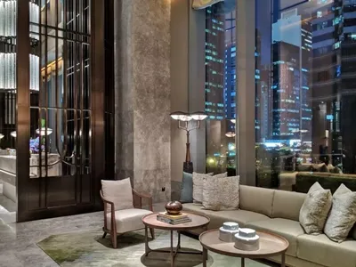 A modern hotel lobby with concrete walls, glass elevators, and a comfortable seating area.