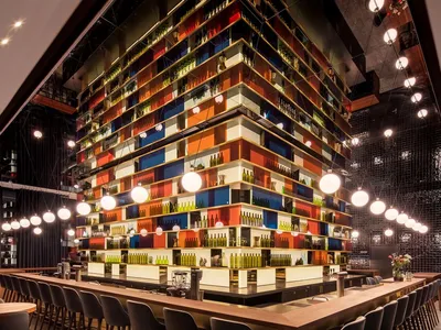 A modern restaurant interior with wooden tables and chairs, colorful shelves, and hanging lights.