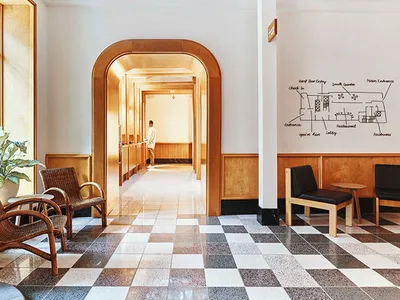 A spacious, terrazzo-floored and wood-paneled hospitality interior with a seating area and a hallway leading deeper into the