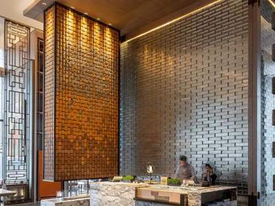 Modern hotel lobby featuring a marble, brick, and concrete design with a reception desk and seating area.