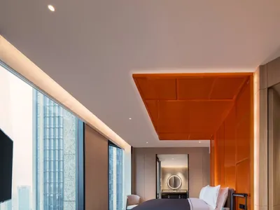 Modern hotel room with a bed, coffee table, and open city view through large windows.