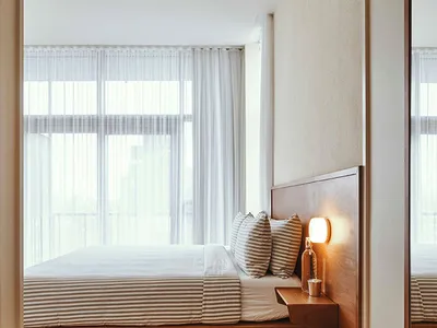 A modern minimalist bedroom featuring a wood-finished platform bed with striped bedding and a floating nightstand.