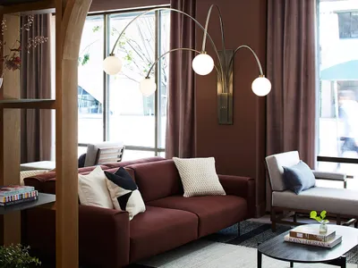 A cozy, industrial-style living room with a deep red sofa, white and black pillows, and a large floor lamp with multiple bulb