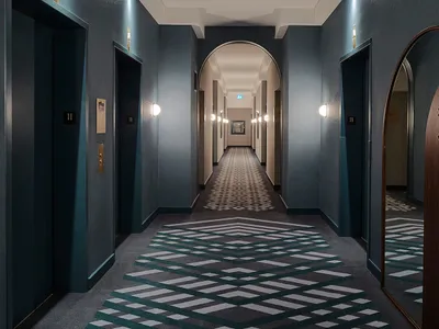 A modern hotel hallway featuring a patterned carpet and wooden accents.