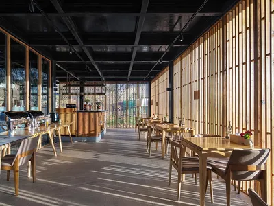 Modern restaurant interior featuring wooden tables and chairs, with large windows allowing natural light to filter in.