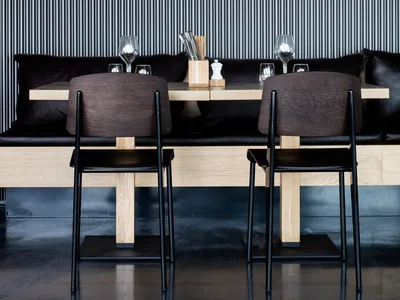 A modern restaurant interior featuring wooden tables and black leather seating.