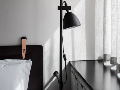 A minimalist bedroom featuring a concrete headboard and a black floor lamp.