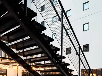 Modern industrial hotel lobby with a black metal staircase, glass walls, and concrete floor.