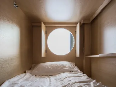 A minimalist bedroom with a bed and a round window in the ceiling, made of wood.