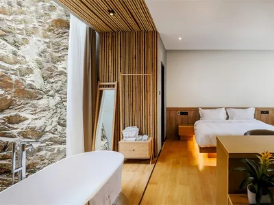 Modern minimalist bedroom featuring a wooden bed and floor, with natural light streaming through a large window and a stone w