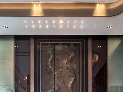 Modern hotel reception area with marble floor and desk, featuring a large sculptural wall art piece.