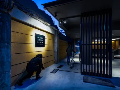 A minimalist hotel interior with a concrete theme, featuring a cyclist and a sign for the Ninja Black Hotel.