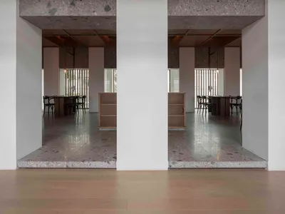 Modern restaurant interior with concrete floors and walls, featuring tables and chairs.