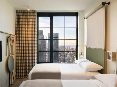 A modern hotel room featuring a city view, textiles, and a large window.
