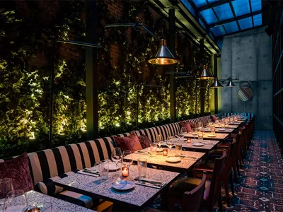 Modern restaurant with concrete, brick, and wooden elements featuring long tables and plush seating.