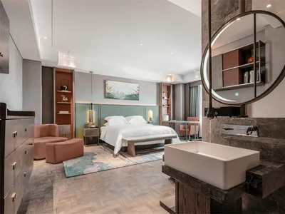 Modern bedroom with minimalist furniture, a large round mirror, a comfortable bed, and a vanity area with a rectangular sink