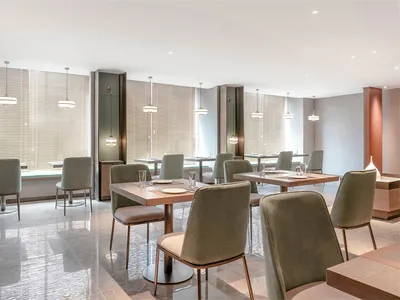 Modern minimalist design of a restaurant dining room with beige walls, wooden furniture, and pendant lights.