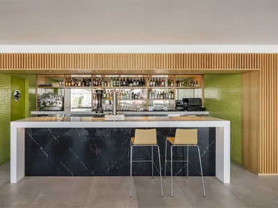Modern bar with black marble counter, timber shelves, and vibrant green accents.