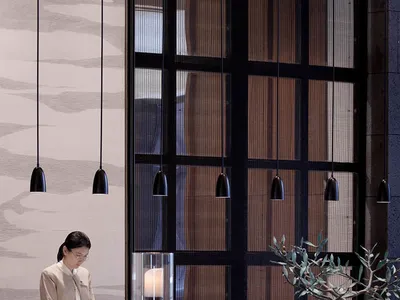 A minimalist modern hotel lobby with wooden elements and hanging lights.