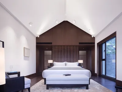 A minimalist bedroom with a large white bed, wooden headboard, and glass panels.