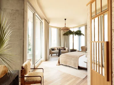 A modern minimalist bedroom featuring a white bed with a wood frame and white walls, complemented by a wooden floor with a bl