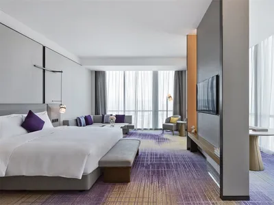 Modern hotel room with a large bed, sofa, television, and floor-to-ceiling windows.